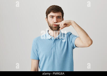 Je ne veux pas raser. Portrait de l'homme drôle positive barbu, debout avec sérieux, les sourcils tout en maintenant l'index au-dessus du nez comme c'est de la moustache sur fond gris Banque D'Images