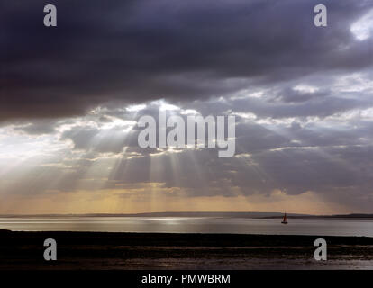 Le soleil qui rayonne à travers les nuages sombres sur la rivière Blackwater près de Waterside Bradwell dans l'Essex. Banque D'Images