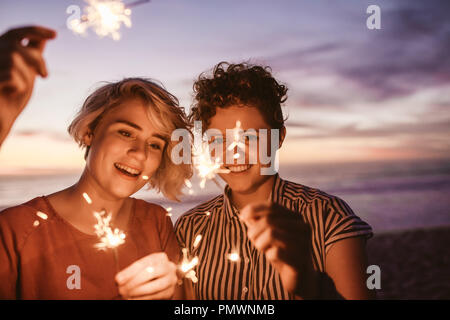 Deux rire young female friends having fun with sparklers debout ensemble sur une plage au crépuscule Banque D'Images