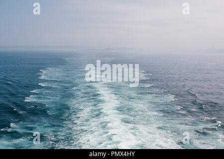 Le service derrière un grand bateau de croisière qu'il quitte le port en eau libre (mer, océan) avec le pays lointain en arrière-plan Banque D'Images