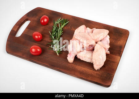 Ailes de poulet crues sur une planche à découper sur fond blanc. Banque D'Images