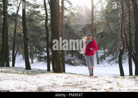 Female runner jogging en forêt d'hiver froid chaud portant des vêtements et des gants d'exécution sportive. Banque D'Images