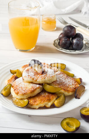 Crêpes au fromage dans du sucre en poudre avec les prunes fraîches sur une assiette. Banque D'Images