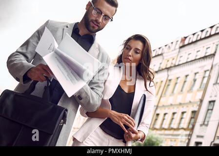 La préparation de réunion. Deux jeunes gens d'affaires à l'extérieur sur la rue de la ville à travers des documents de lecture concentrée fond voir close-up Banque D'Images
