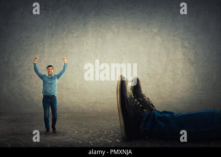 Une happy businessman with arms raised up célèbrent la victoire contre son patron géant tombé. Confrontation Bureau combattre la concurrence, w inattendues Banque D'Images