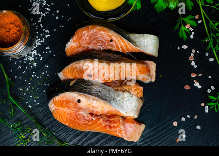 Truites fraîches ou des darnes de saumon aux épices, aneth, citron dans un bocal en verre, poivre, épices à Fort rouge, rose et de sel blanc sur fond de bois, prête à cuire Banque D'Images