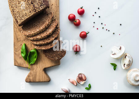 Mise à plat avec le pain sur la planche à découper en bois, de poivre noir et de légumes pour la cuisine petit-déjeuner sur la surface en marbre blanc Banque D'Images
