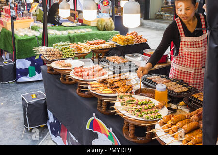 Woman cooking brochettes grillées de viande et de poisson pour la vente à un marché de rue dans la région de Bangkok, Thaïlande Banque D'Images