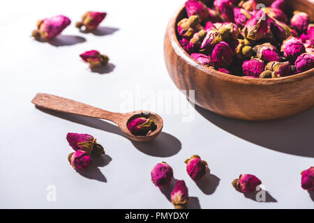 Boutons de rose séchés dans bol en bois et sur la cuillère de table blanc Banque D'Images