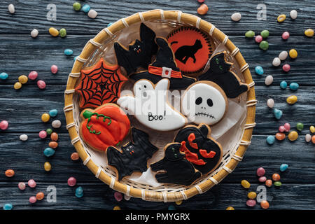 Vue de dessus du panier en osier avec des Spooky Halloween cookies entouré de bonbons sur table en bois Banque D'Images