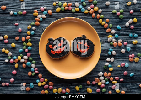 Vue du dessus de la plaque avec les cookies d'halloween entouré de bonbons colorés sur table en bois Banque D'Images