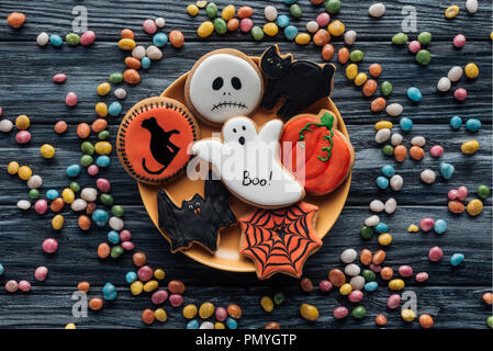 Vue du haut de la plaque à biscuits halloween entouré de bonbons colorés sur table en bois Banque D'Images