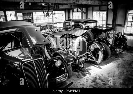 Vue arty, en noir et blanc des voitures classiques d'époque garées côte à côte, exposées dans un garage ouvert, prises d'un angle élevé. Banque D'Images