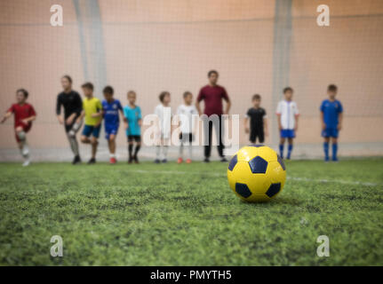 Ballon de football traditionnel sur le terrain de football sur l'arrière-plan d'enfants joueurs et leur entraîneur de football Banque D'Images