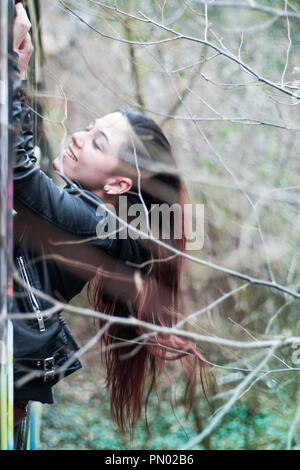 Jeune brunette woman hanging out d'une fenêtre de train abandonné dans les bois avec de longs cheveux rouges Banque D'Images