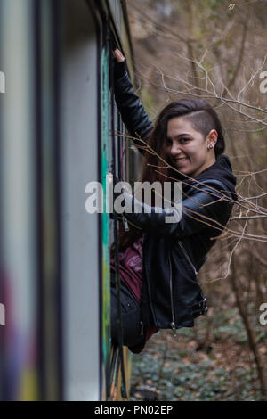 Jeune brunette woman hanging out d'une fenêtre de train abandonné dans les bois avec de longs cheveux rouges Banque D'Images