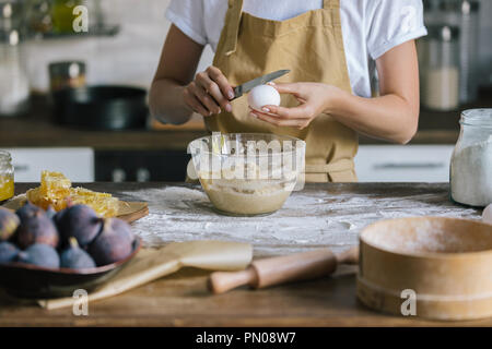 Cropped shot of woman in apron briser dans le bol d'oeufs au cours de préparation tarte Banque D'Images