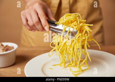 Cropped shot of woman putting spaghetti sur la plaque avec des pinces Banque D'Images