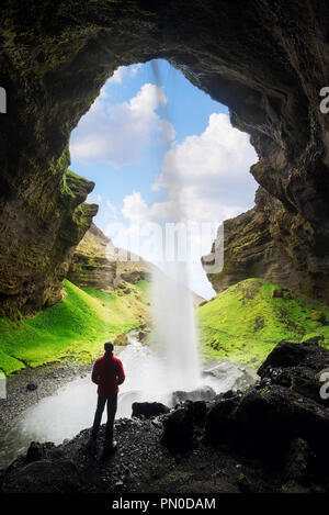 Kvernufoss cascade dans les gorges de la montagne. L'attraction touristique de l'Islande. Man in red jacket debout et s'intéresse à l'écoulement de l'eau qui tombe. Bea Banque D'Images