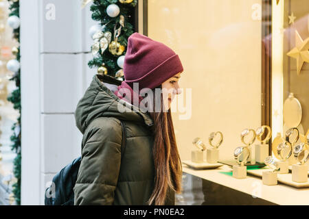 Une belle jeune femme ou une jeune fille regarde la vitrine et choisit un cadeau de Noël. Banque D'Images