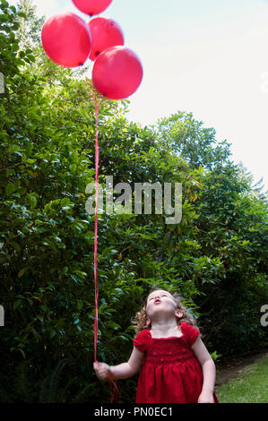 Une jeune fille dans une robe rouge holding balloons. Banque D'Images