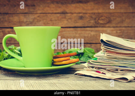 Tasse de thé, de menthe, cookie, tas de journaux et magazines sur fond de bois. La tonalité de l'image. Banque D'Images