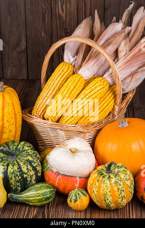 Motif de l'action de l'automne avec un panier plein d'épis de maïs et les différentes citrouilles coloré sur un vieux fond de bois rustique Banque D'Images