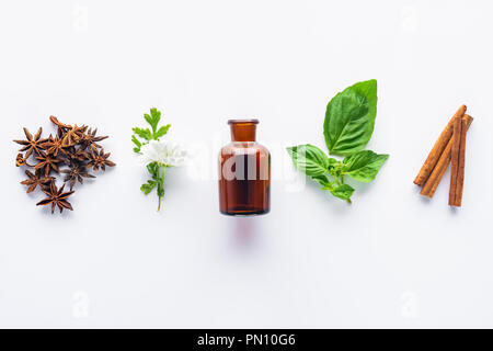 Portrait de bouteille d'huile essentielle aromatique, des bâtons de cannelle, oeillet et vert feuilles isolées sur fond blanc Banque D'Images