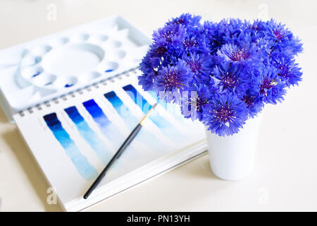 Diverses peintures aquarelle bleu dans la palette et sur papier. Avec un vase de fleurs bleu bouton baccalauréat. Banque D'Images