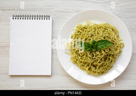 Plat de pâtes spaghetti avec sauce pesto et blank notepad, vue du dessus. Les frais généraux, de dessus, de mise à plat. L'espace pour le texte. Banque D'Images