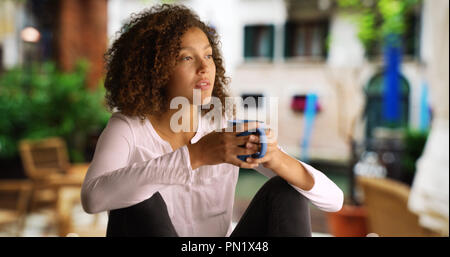 Jolie femme noire avec des cheveux bouclés se trouve en dehors de boire du café Banque D'Images