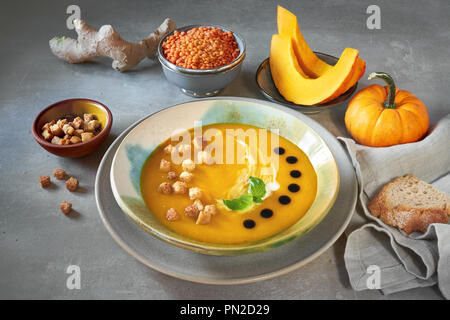 Potage à la citrouille savoureux servi avec des croûtons, de la crème et le vinaigre balsamique dans un bol en céramique. Tranches de citrouille, des lentilles rouges, d'épices et les feuilles de basilic sont Banque D'Images