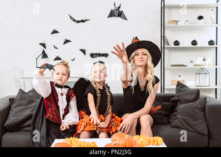 Portrait de Mère et enfant dans un costume d'halloween de jeter le papier noir chauve-souris à la maison Banque D'Images