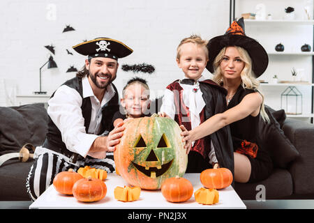 Portrait of smiling family dans divers costumes de Halloween à table de café avec des citrouilles à la maison Banque D'Images