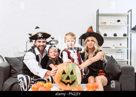 Portrait de famille dans divers costumes de Halloween à table de café avec des citrouilles à la maison Banque D'Images