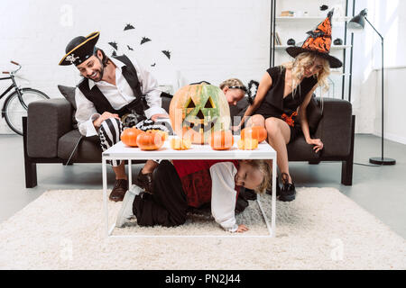 Petit garçon se cachant de parents et sa sœur dans un costume d'halloween avec des citrouilles sous la table à la maison Banque D'Images