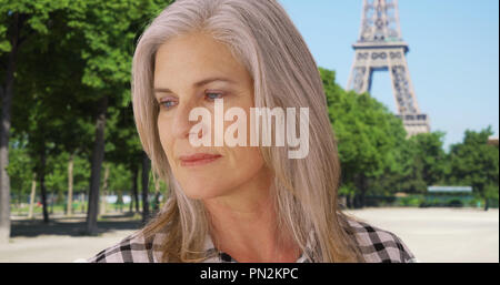 Femme plus âgée regarde vers le bas alors qu'il se tenait près de la Tour Eiffel Banque D'Images