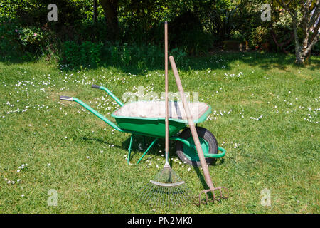 Brouette verte avec pelouse et râteau cultivateur griffe dans un jardin Banque D'Images