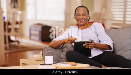 Une vieille femme noire heureusement utilise sa tablette en regardant la caméra Banque D'Images