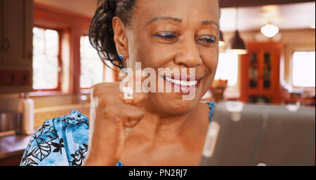 Une vieille femme afro-américaine utilise sa tablette dans sa cuisine Banque D'Images