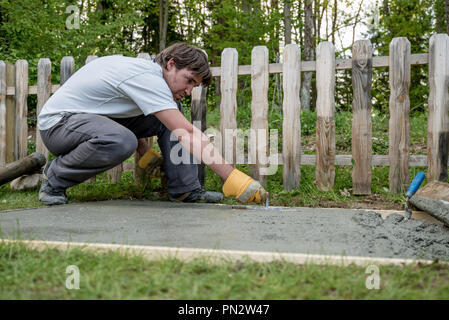 Concept DIY - jeune homme frais de mise à niveau de plancher de béton à l'aide d'un maillet dans son arrière-cour. Banque D'Images
