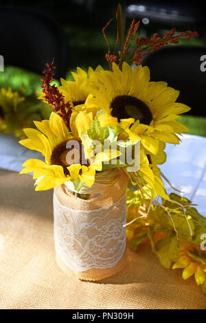 Pot couvert de dentelle et de jute remplis de faux tournesols situé sur une table couverte de tissu blanc et toile Banque D'Images