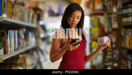 Femme noire au contrôle du marché du thon en conserve la valeur nutritive on cellphone Banque D'Images