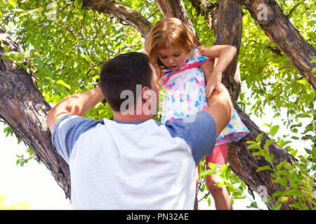 Père aide sa fille à sortir d'un arbre Banque D'Images