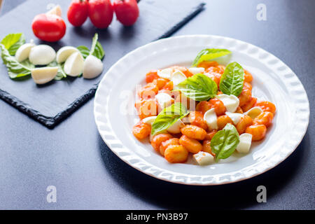 Gnocchi alla Sorrentina en sauce tomate avec basilic frais et vert en tranches de mozzarella balls servi sur une plaque blanche avec des ingrédients sur tableau noir bac Banque D'Images