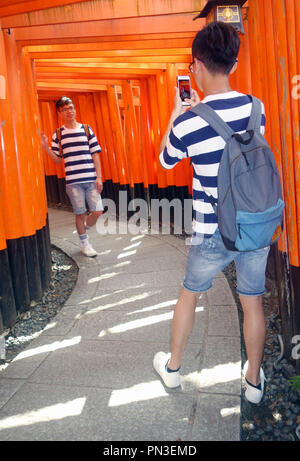 Les garçons en photographiant chaque autres entre red torii gates, sanctuaire Fushimi Inari, Kyoto, Japon. Aucune communication ou MR Banque D'Images