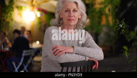 De graves senior woman sitting on outdoor patio de nuit en ville européenne Banque D'Images