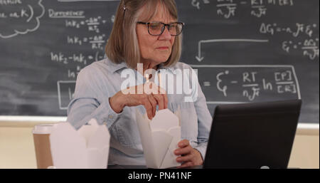 Des femmes âgées enseignant ayant le déjeuner et l'utilisation d'ordinateur portable dans la salle de classe Banque D'Images