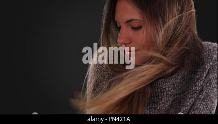 Belle femme avec de longs cheveux bruns dans le vent sur fond gris Banque D'Images