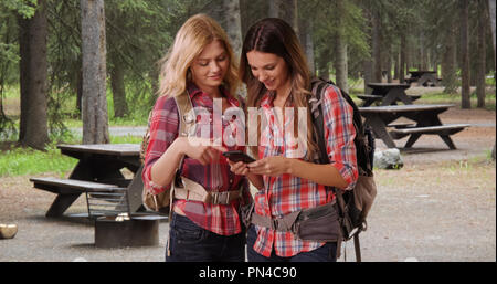 Deux filles de race blanche en utilisant smartphone à forest camping Banque D'Images